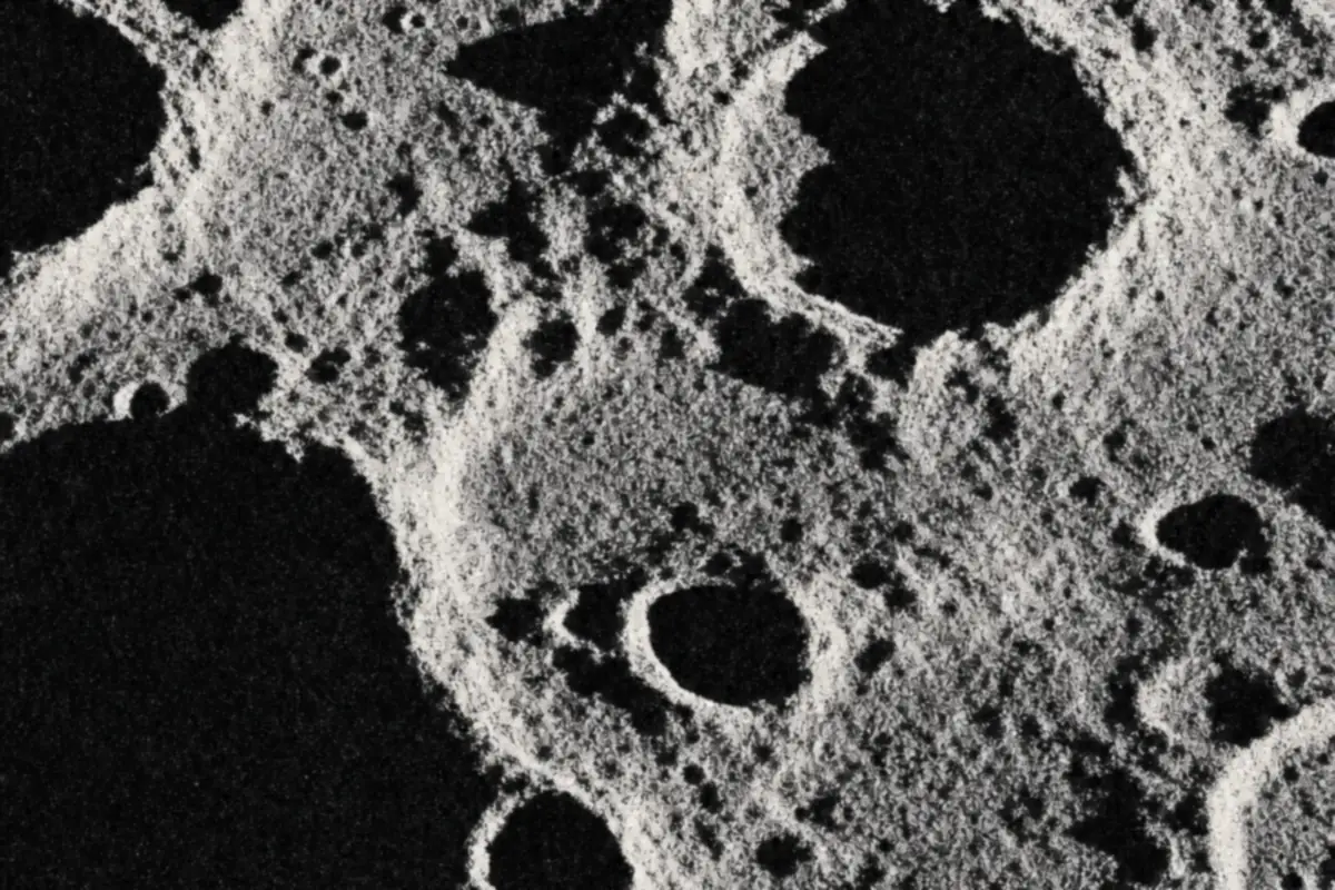 A very close view of the lunar surface in high contrast black and white, with crater rims lit from a low angle and deep black shadows inside the craters.